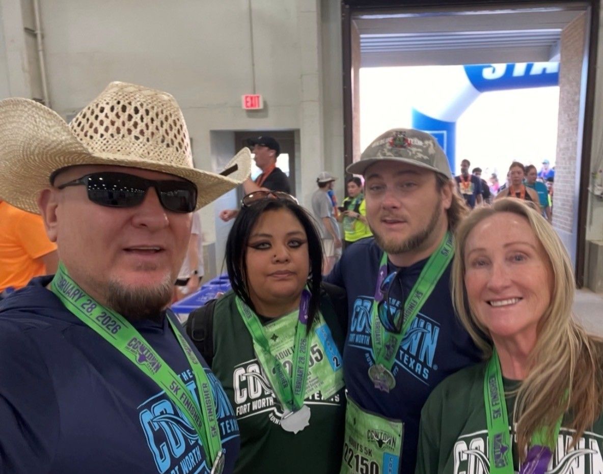Four people wearing green lanyards pose at an indoor event, smiling for a selfie.