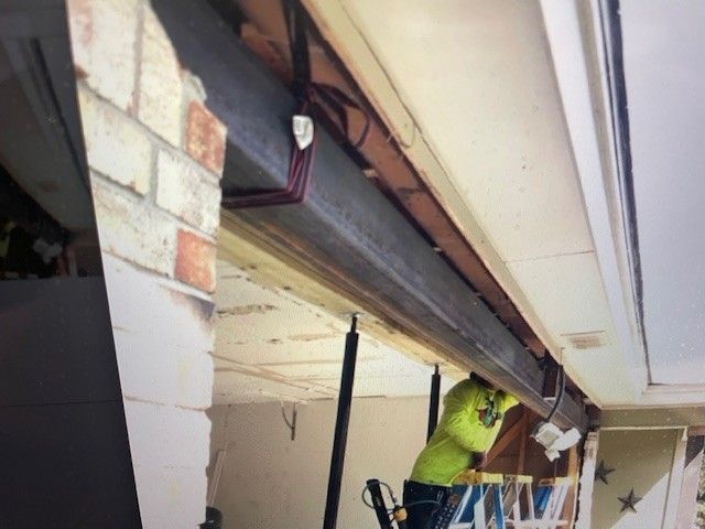 Worker repairing ceiling beams in a room with exposed wood and brick walls