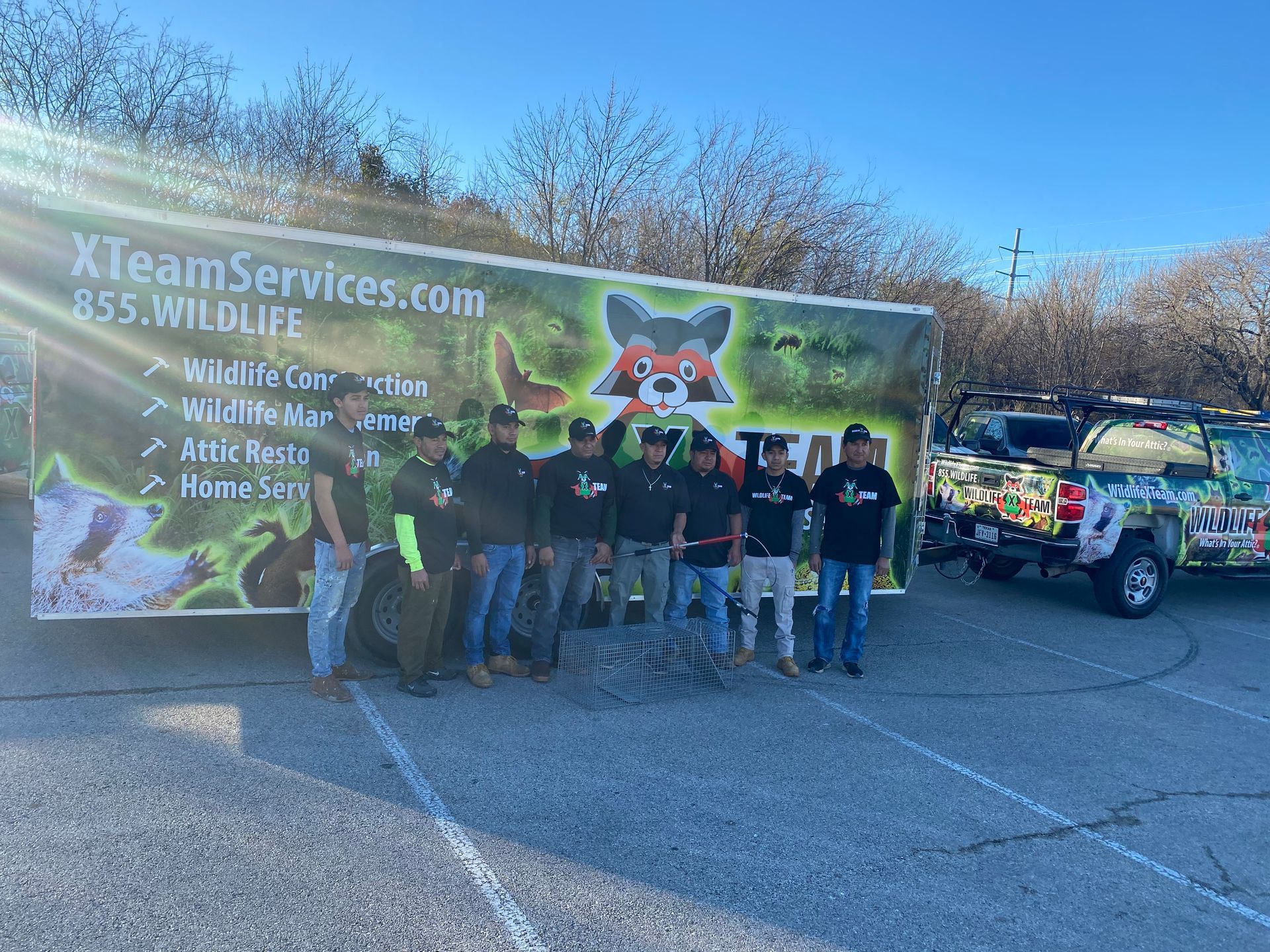 Team of people posing beside a wrapped XTeamServices.com truck in a parking lot, with a colorful banner backdrop.