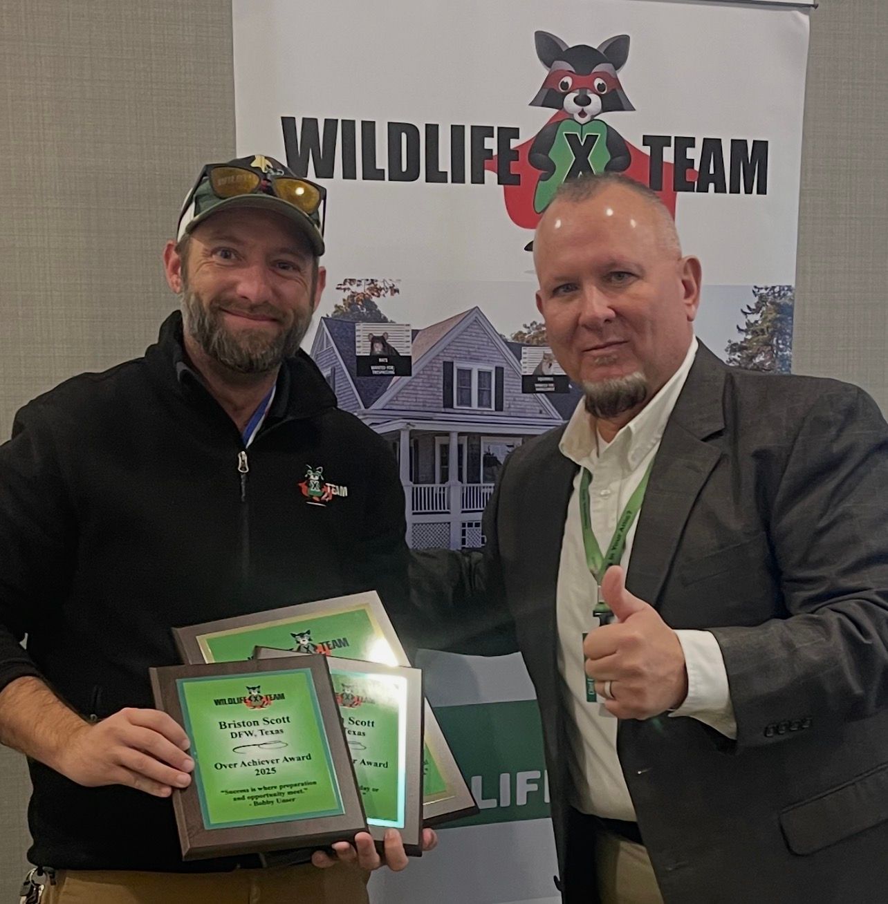 Two men posing with a plaque at a Wildlife X Team event banner