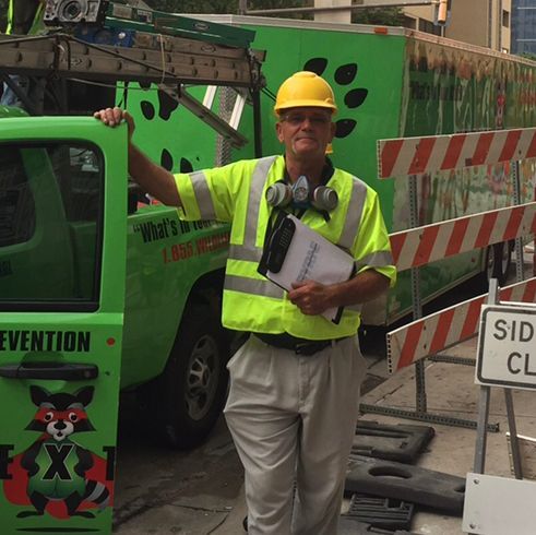 Construction worker in a yellow hard hat and safety vest standing by a green truck at a roadwork site
