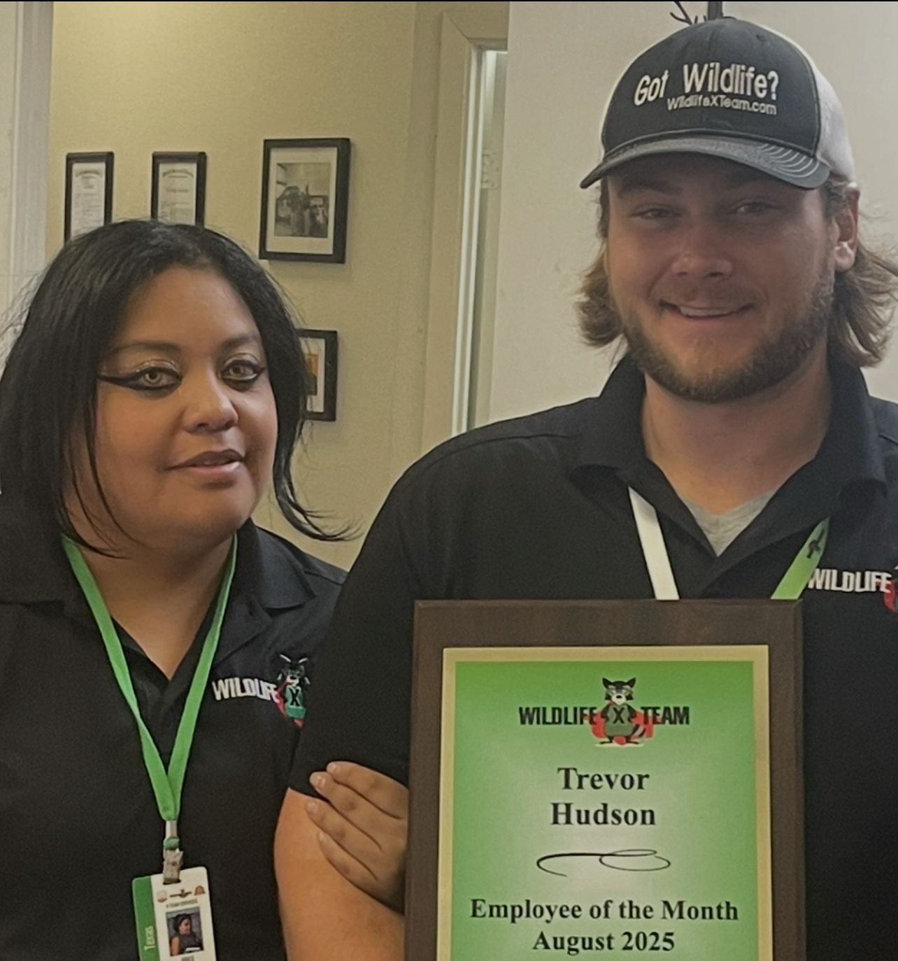 Two staff members hold an “Employee of the Month” plaque at Wildlife X Team.