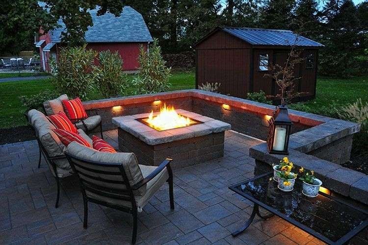 Cozy outdoor fire pit area with seating, fire burning, and decorative lighting.