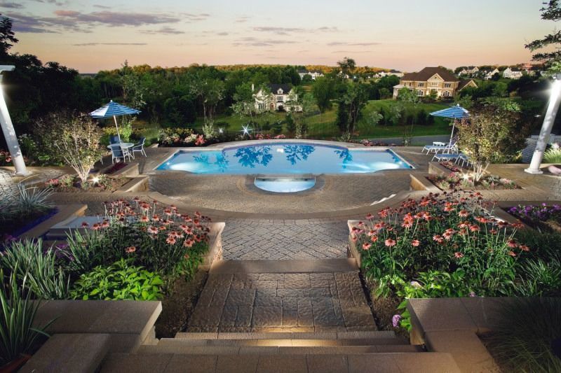 Backyard pool at dusk, surrounded by landscaping, with views of houses and trees in the distance.
