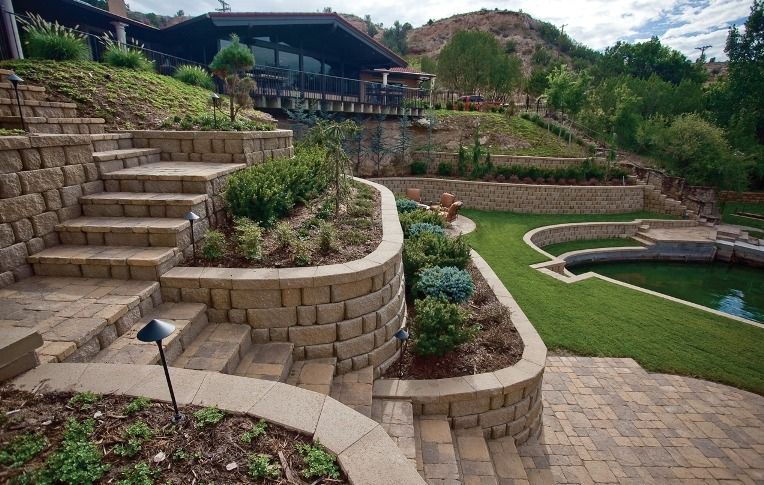 Stone steps and retaining walls in landscaped yard, leading up to a house with a pool.