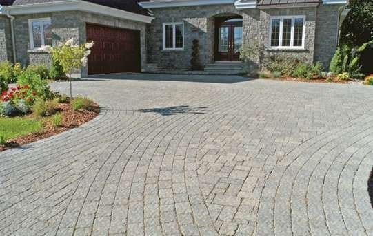 Stone brick driveway curves towards a stone house, with a garage and front door.