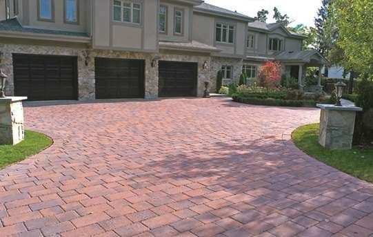 Brick paver driveway leading to a large house with three garage doors.