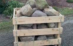 Wooden crate filled with large rocks, outdoors on gravel.