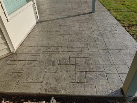 A concrete patio with a brick pattern and a white house in the background