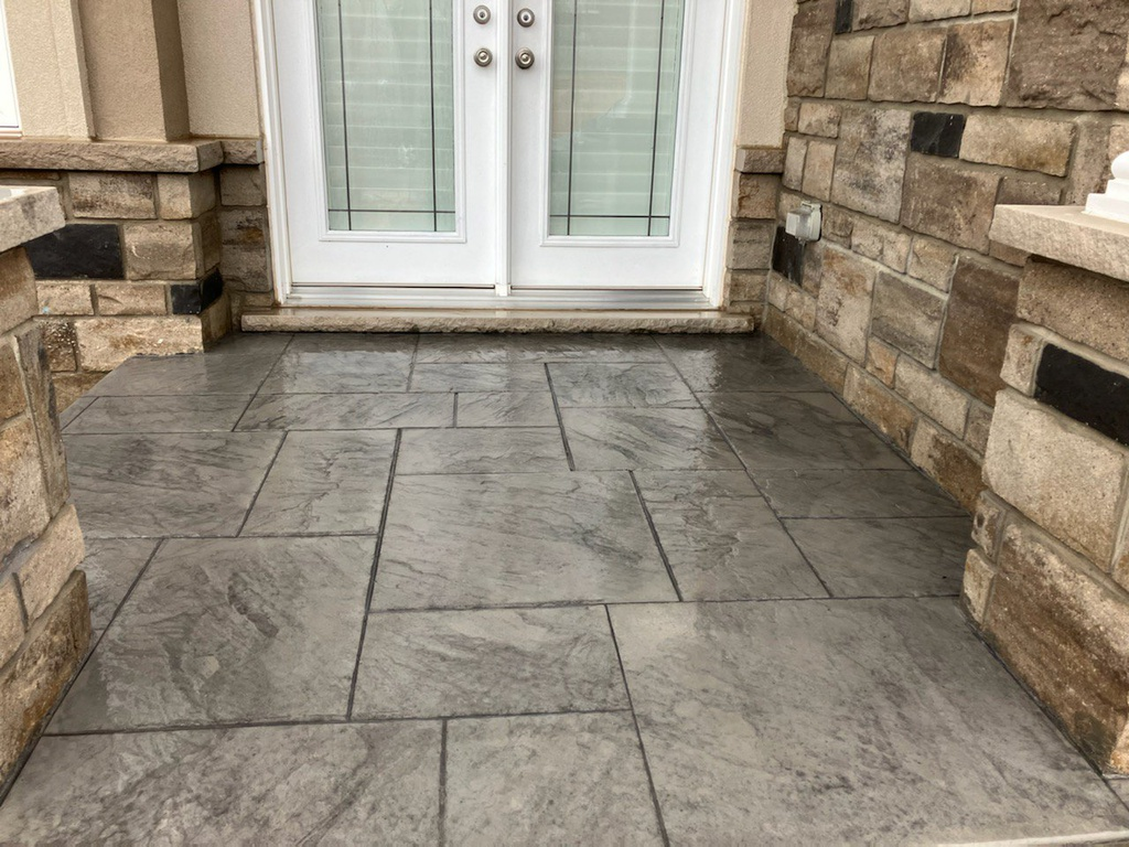 A concrete walkway with a brick wall and a door in the background