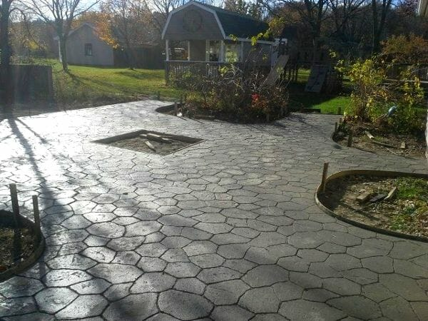 A patio with a fire pit in the middle of it and a house in the background