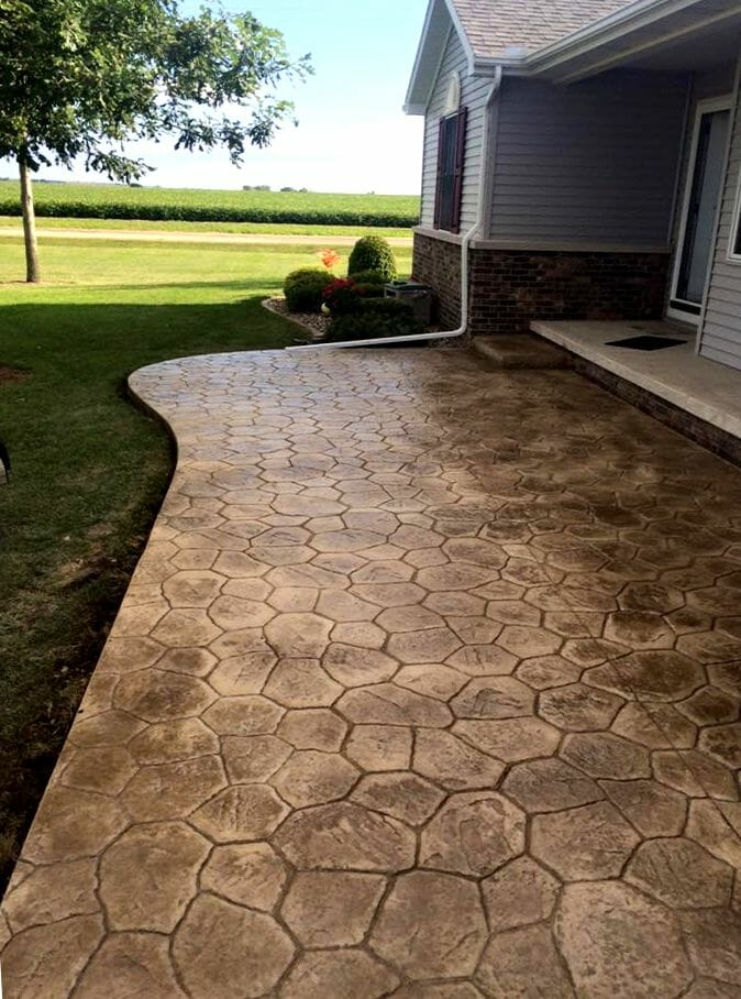 A concrete walkway leading to a house with a field in the background