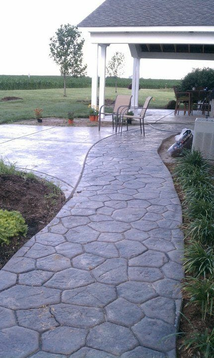A walkway leading to a patio with chairs and a gazebo in the background