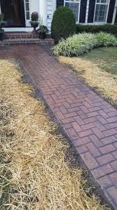 A brick walkway leading to a house with hay on the side of it