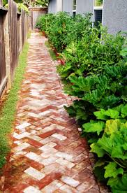 A brick walkway leading to a house surrounded by plants