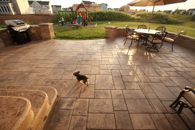 A small dog walking on a patio next to a table and chairs