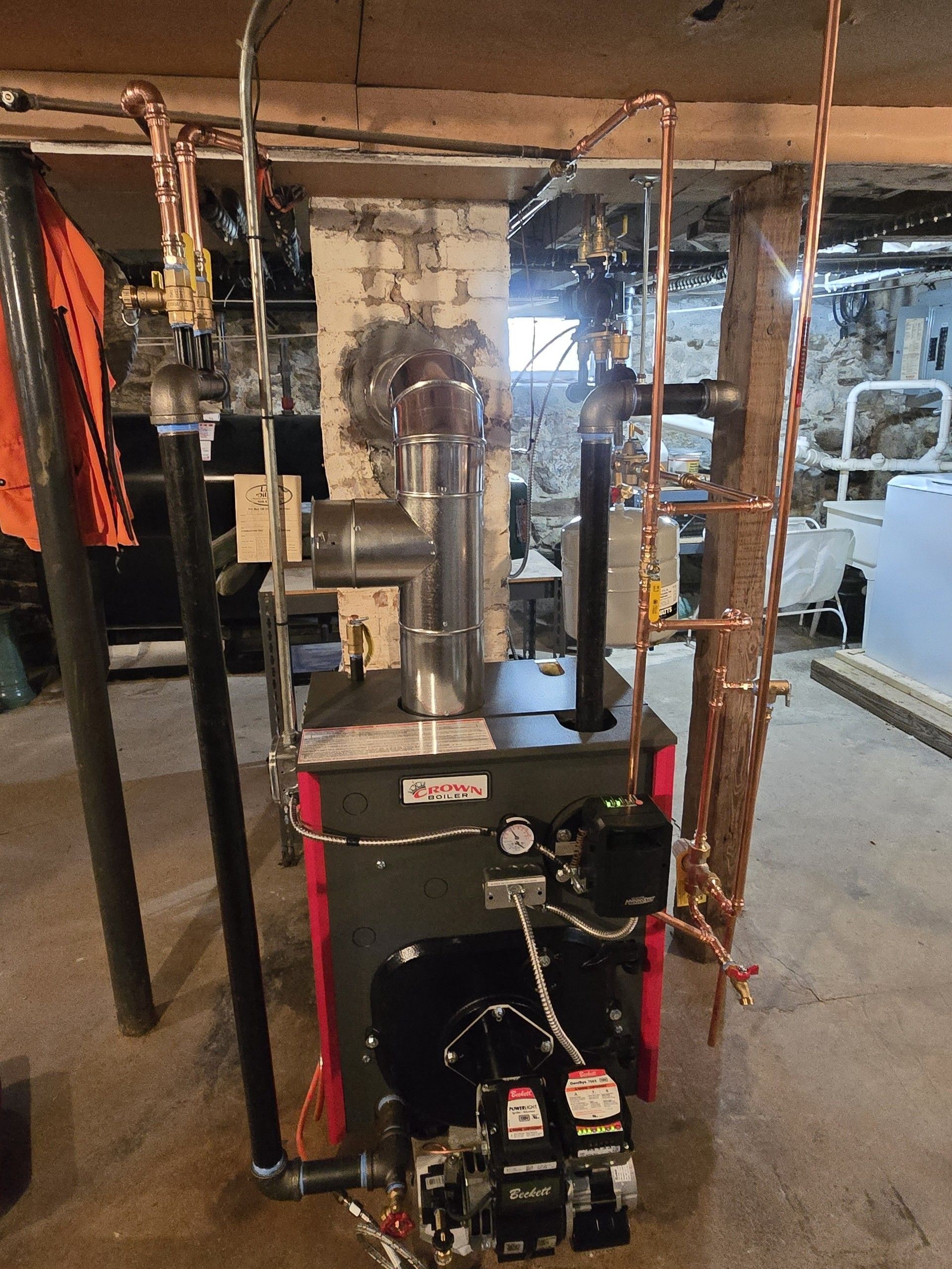 Boiler and heating equipment in a basement utility room, with pipes and exposed framing.