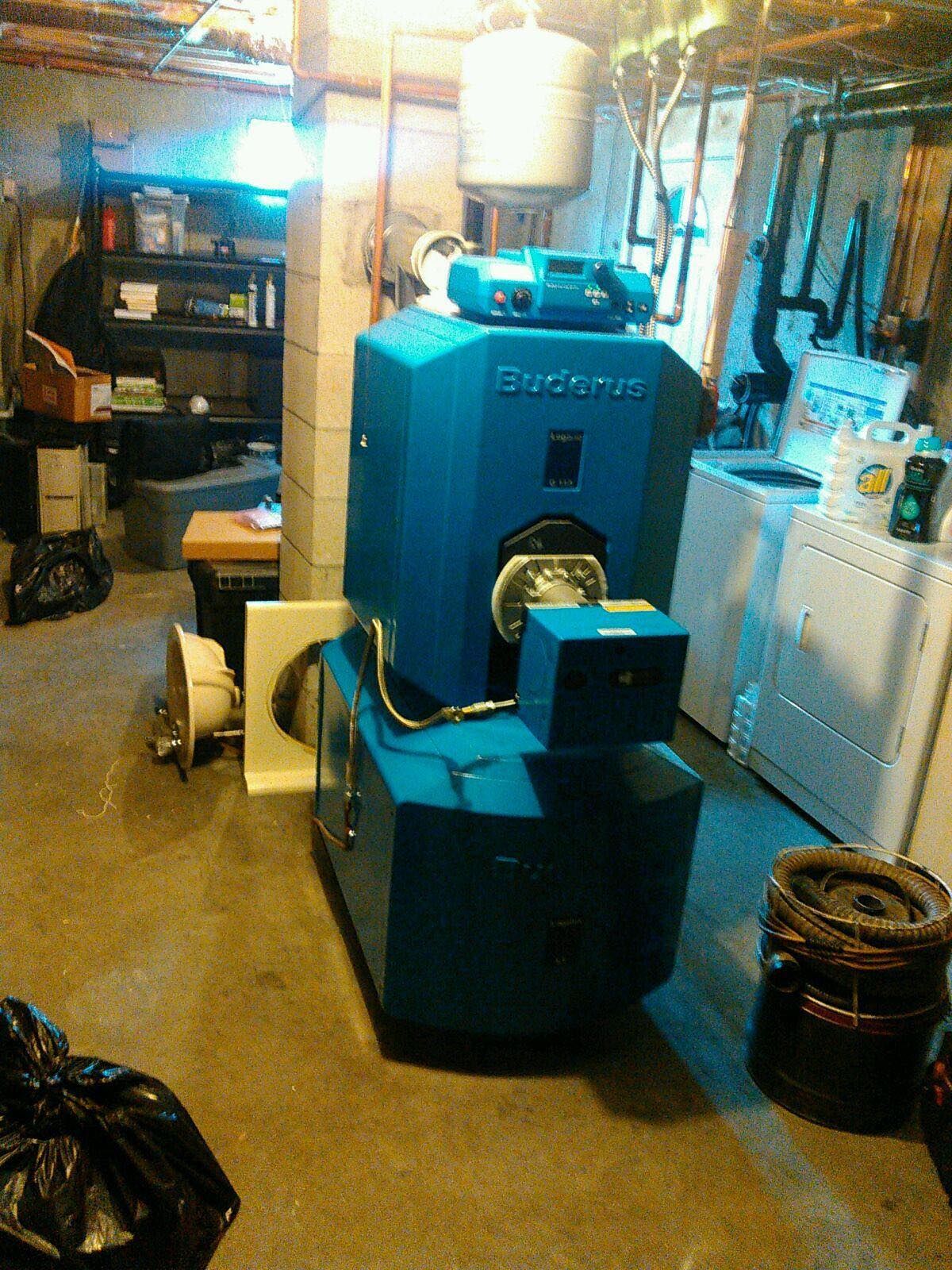 A blue boiler is sitting in a basement next to a washer and dryer.