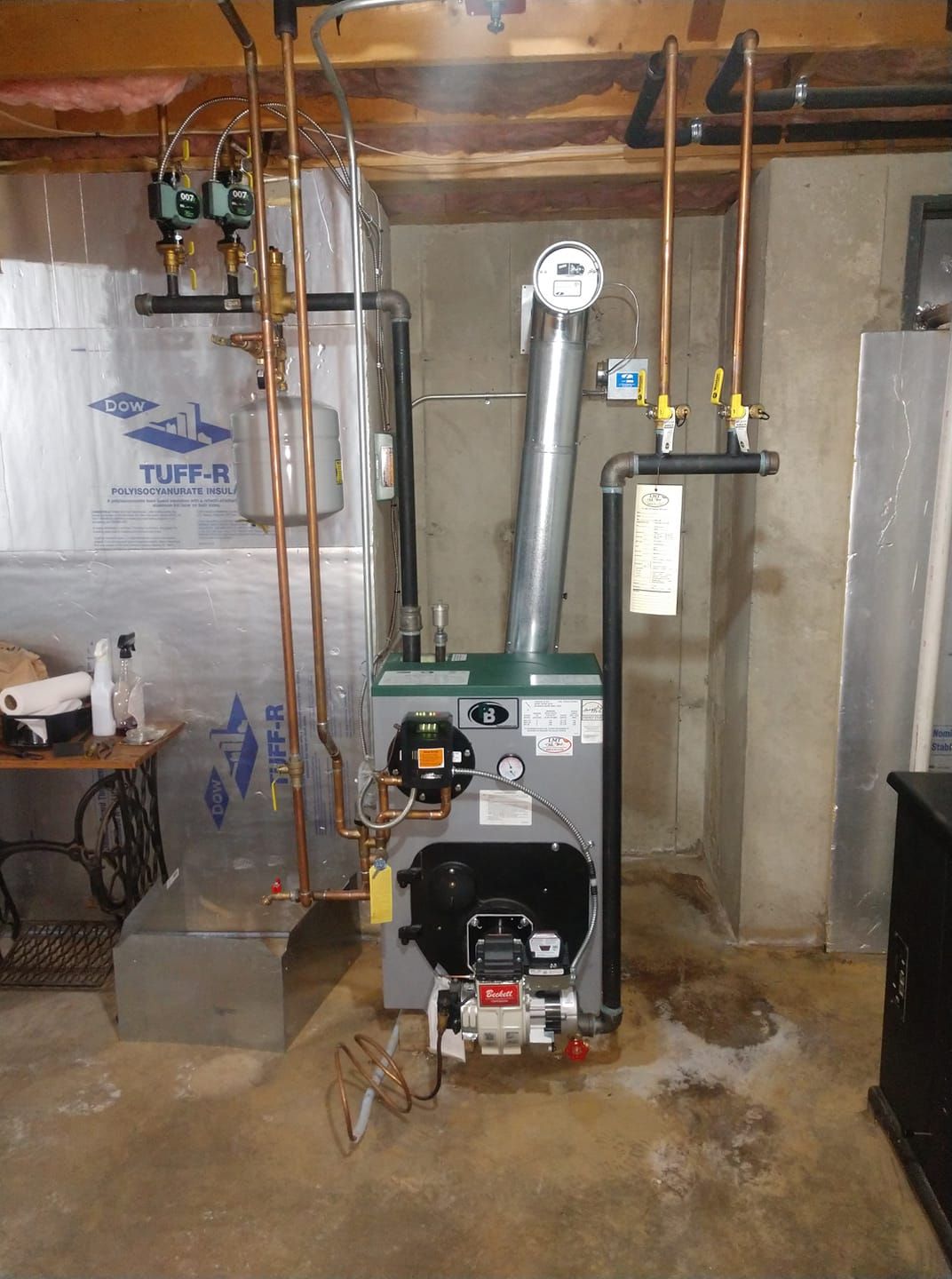 A gas boiler is sitting in a basement next to a wall.