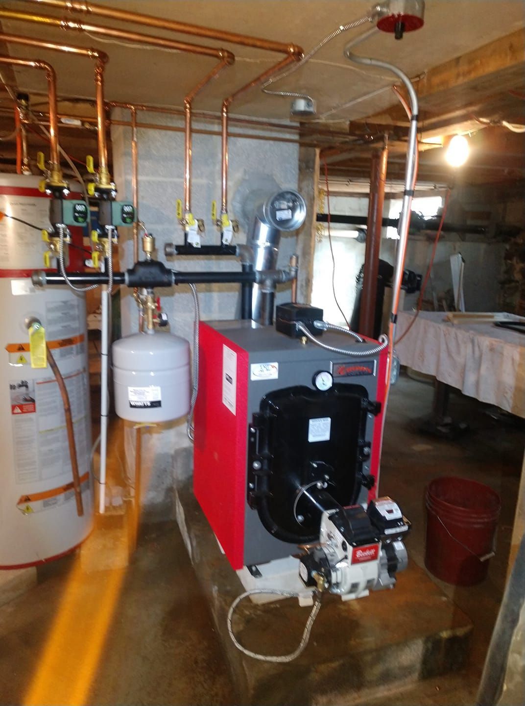 A red and black boiler in a basement with copper pipes