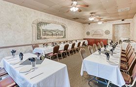 A banquet hall with long tables set for a meal. The walls are painted with a mural and decorations.