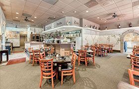 Restaurant interior with tables and chairs set for dining; the open kitchen is in the back.