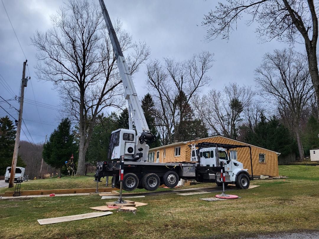 A white crane truck parked on a grassy residential lawn next to a house with exposed framing.
