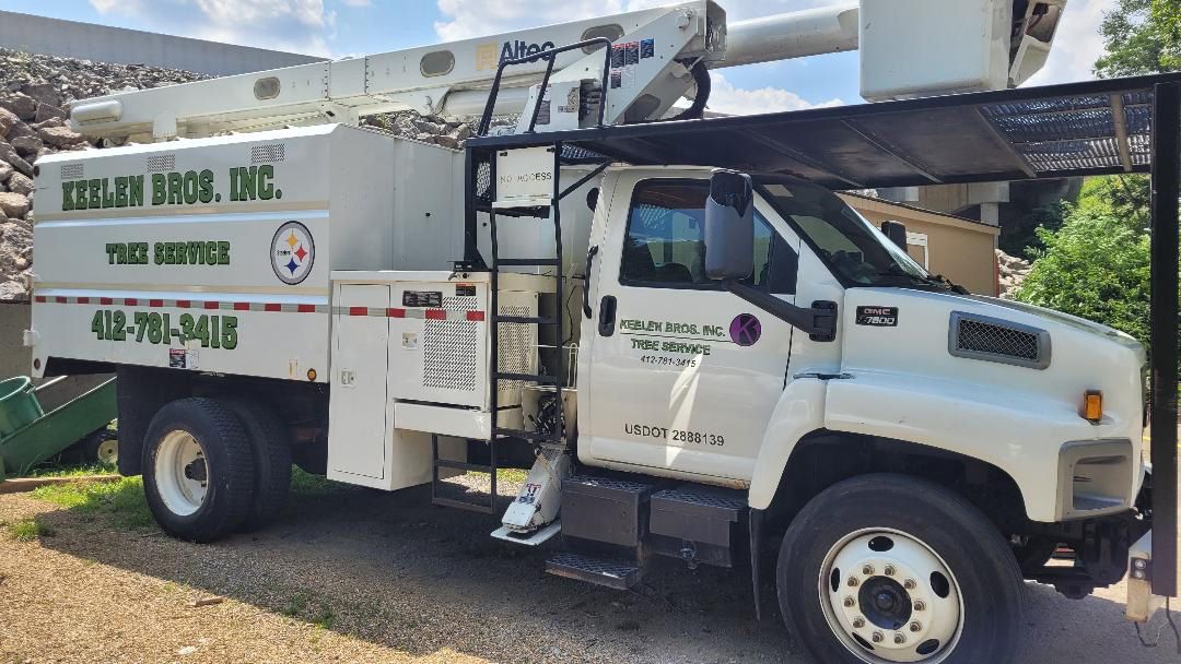 White Keeley Bros. Inc. tree service bucket truck parked on a gravel lot under a partial awning.