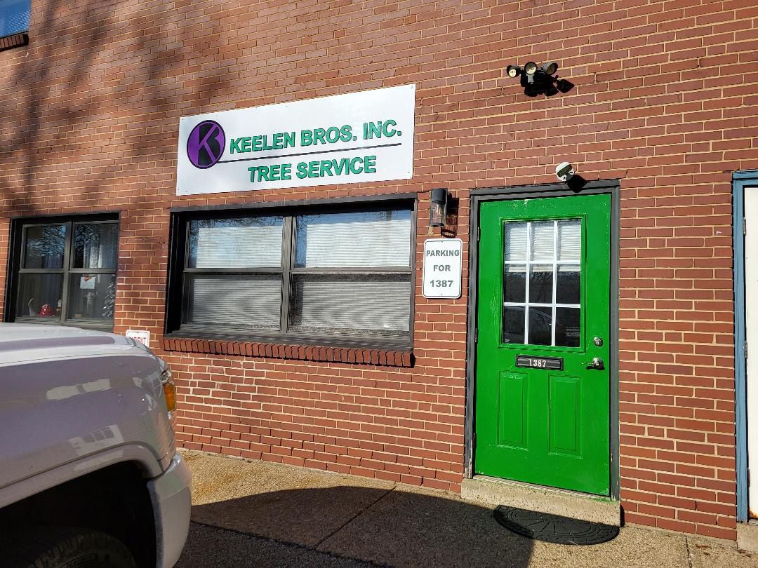 A brick building exterior with a sign for Kehlen Bros. Inc. Tree Service, a large window, and a bright green door.