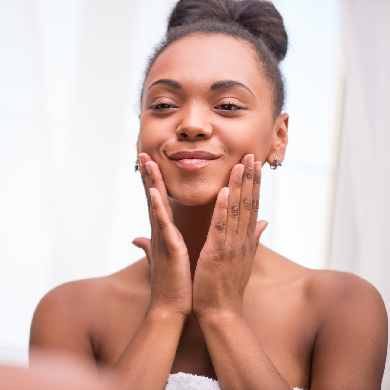 A woman is touching her face in front of a mirror.