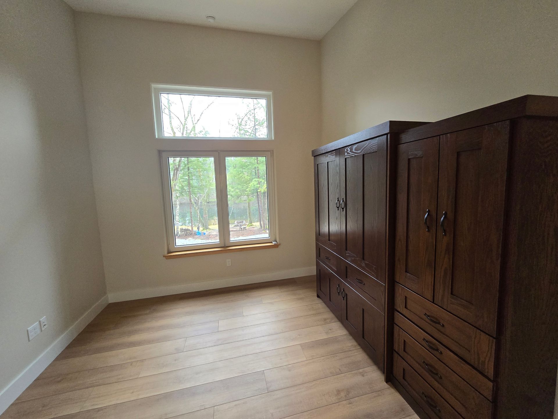 An empty room with a large window and wooden cabinets