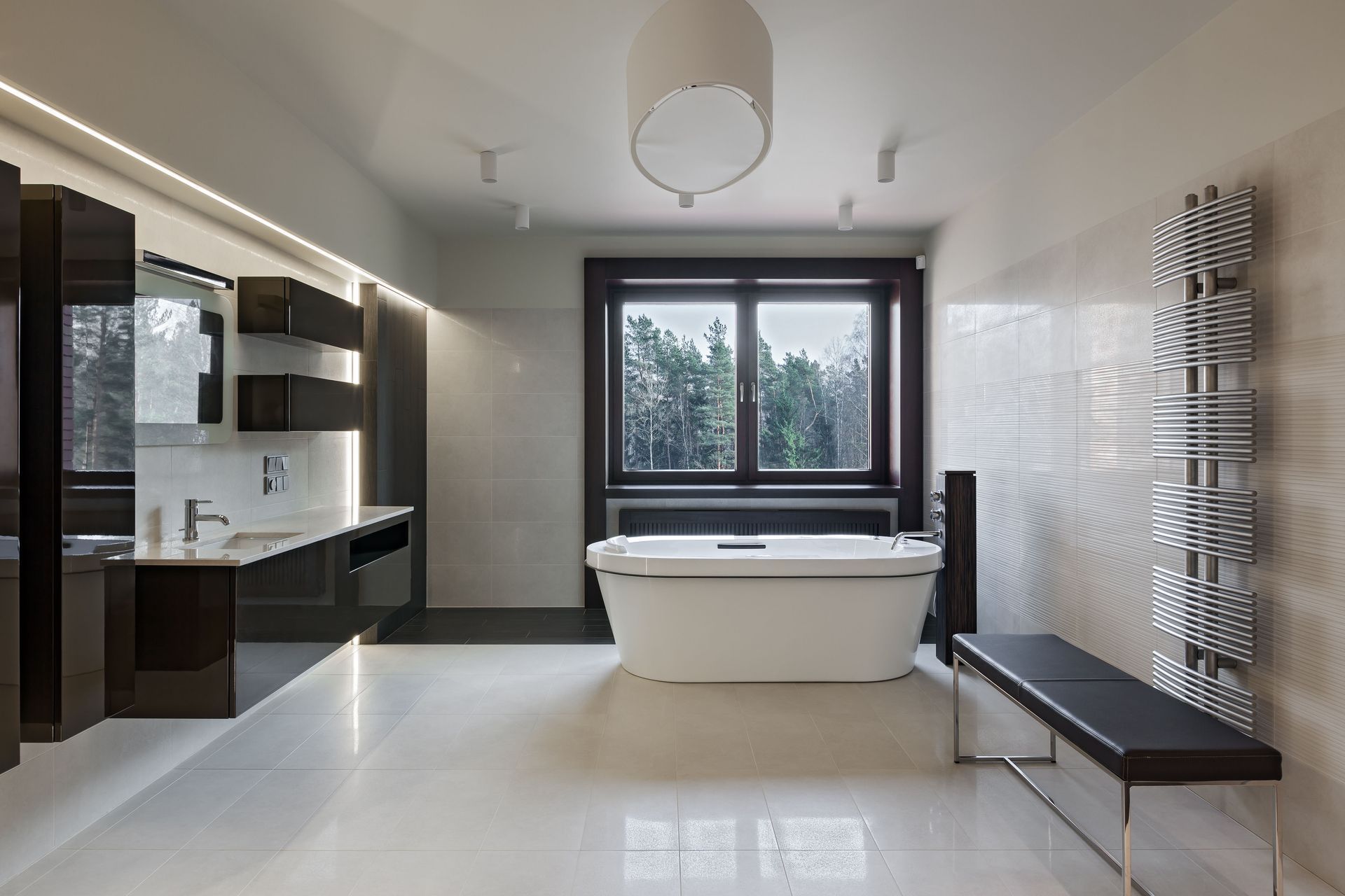 Modern bathroom with white bathtub, dark cabinets, window, and glossy floor.