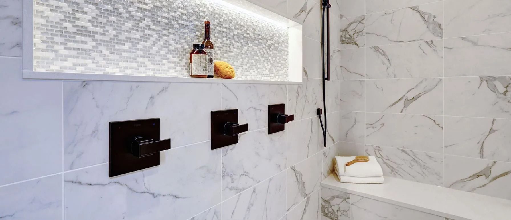 Bathroom with marble-like tile, dark fixtures, and a recessed shelf with toiletries.