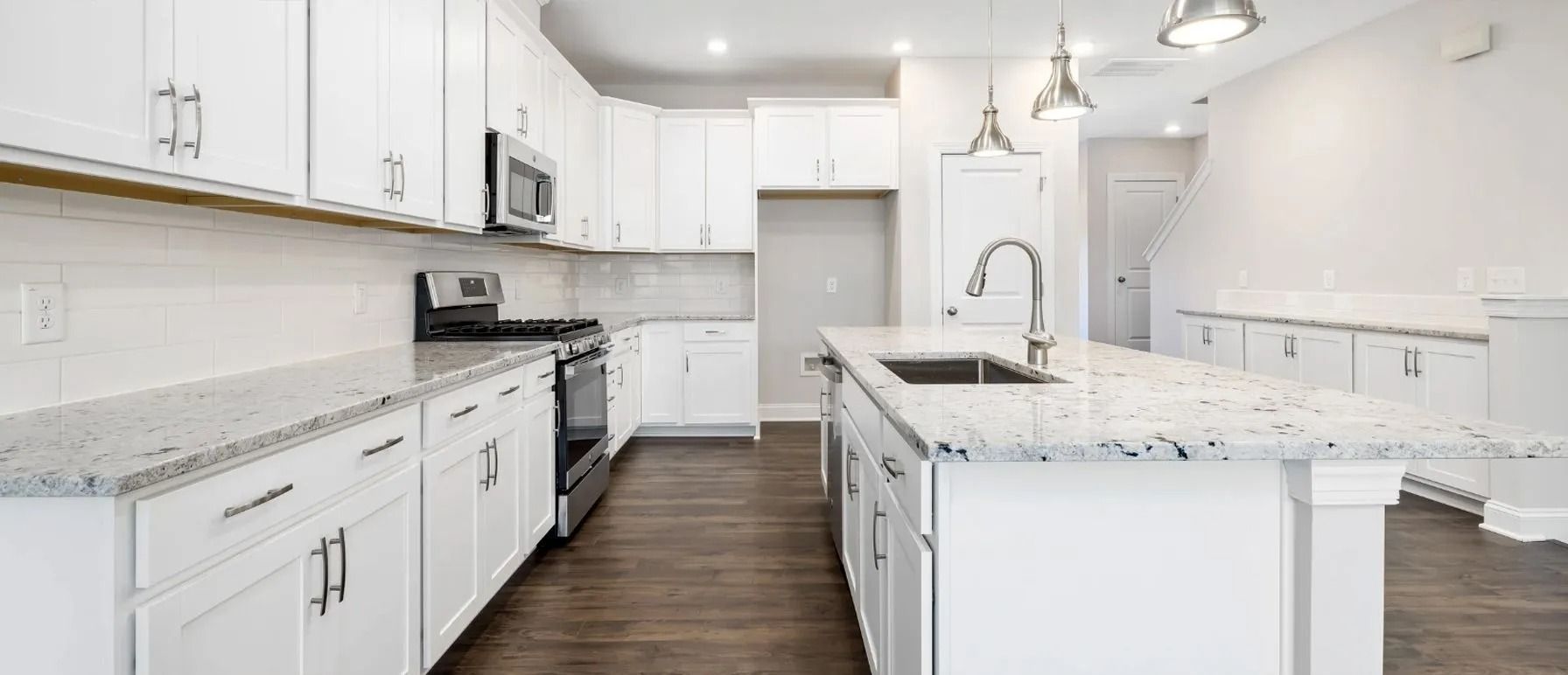 Bright white kitchen with granite countertops, stainless steel appliances, and wood flooring.