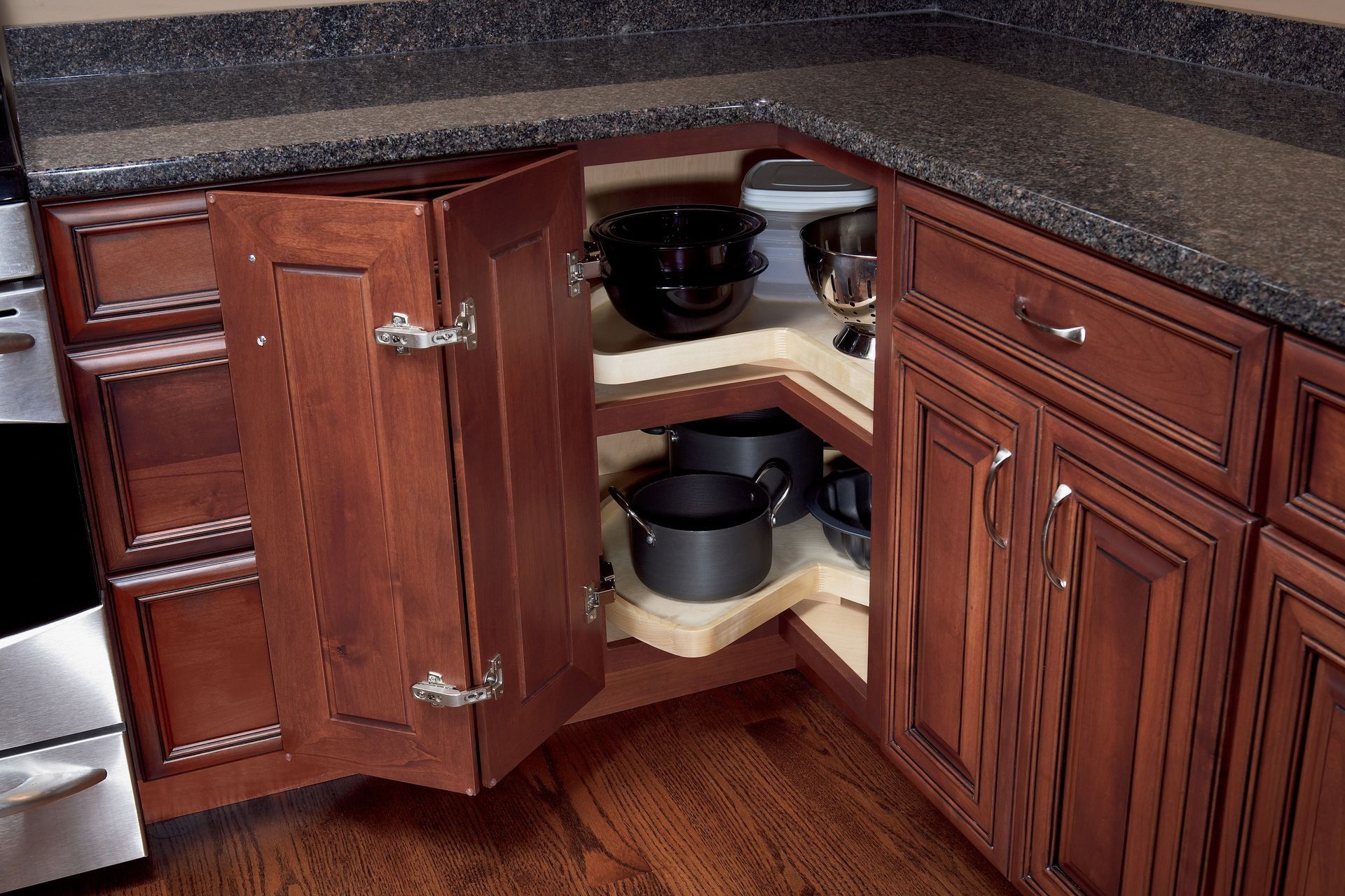 Open corner kitchen cabinet with pull-out shelves holding pots and pans. Dark wood, black countertop.