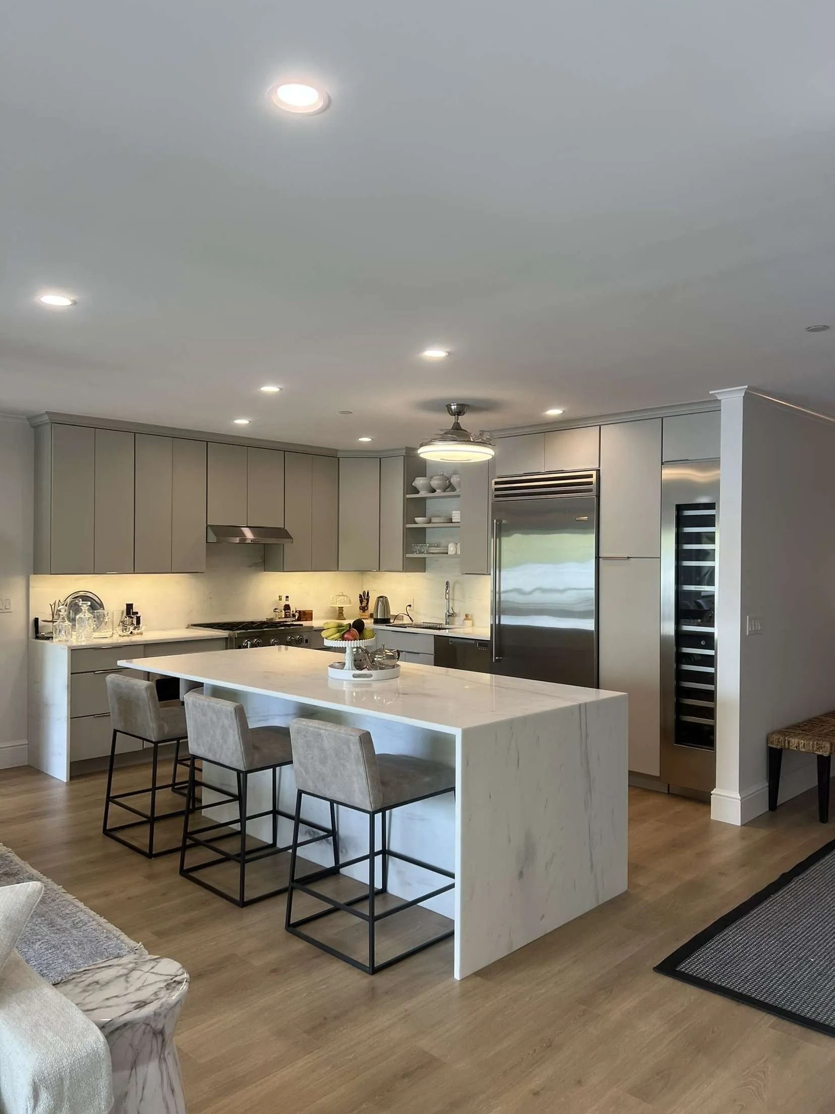 Modern kitchen with white island, gray cabinets, stainless steel appliances, and wood floors.