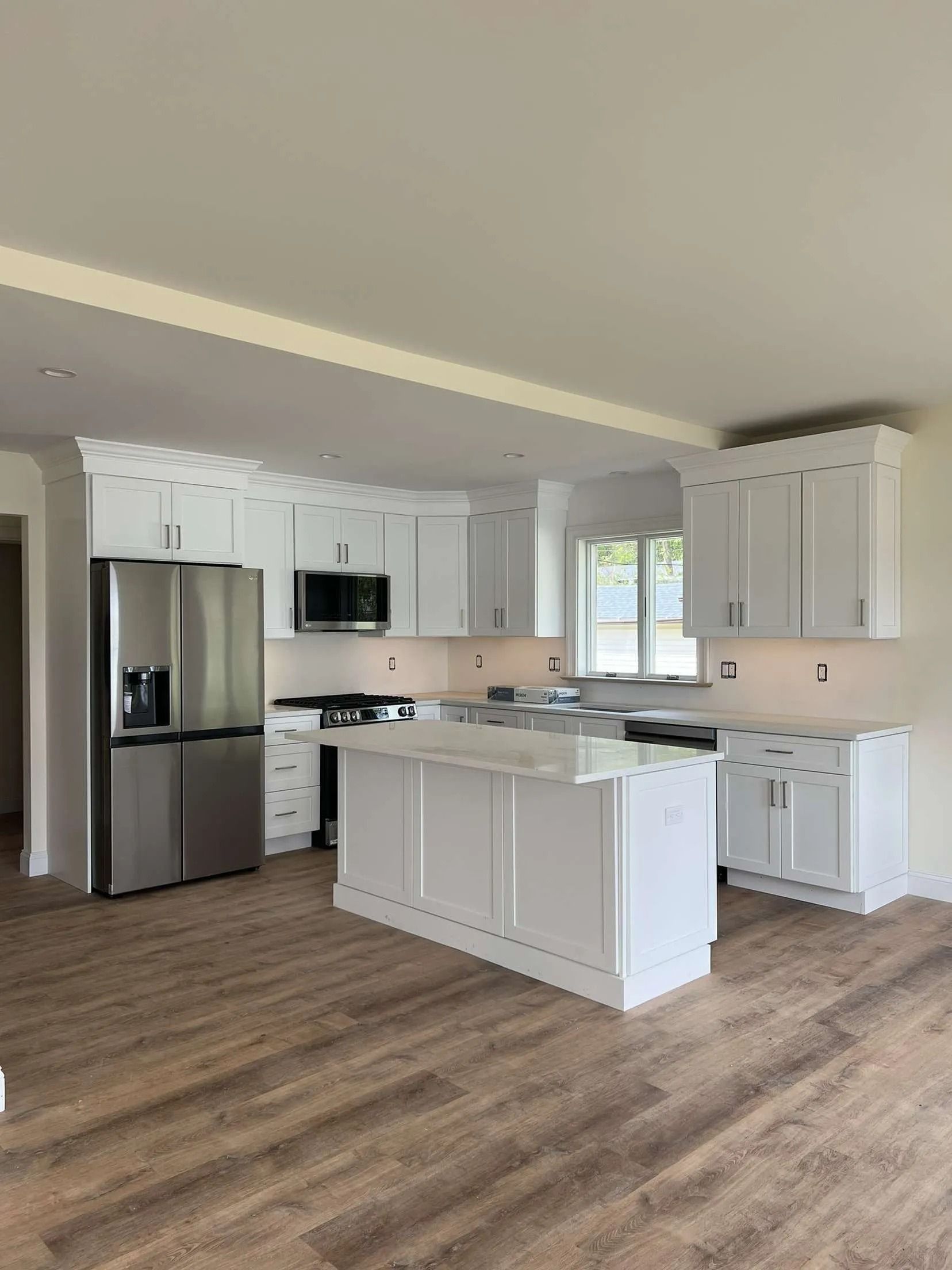 White kitchen with island, stainless steel refrigerator, and wood-look flooring.