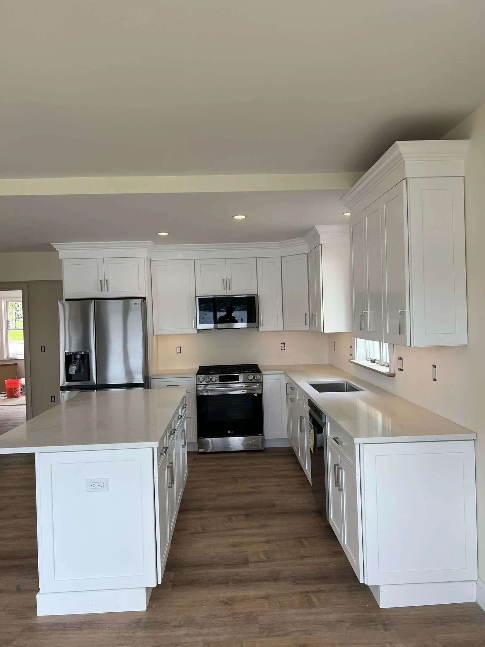 White kitchen with an island, cabinets, stainless steel appliances, and wooden flooring.