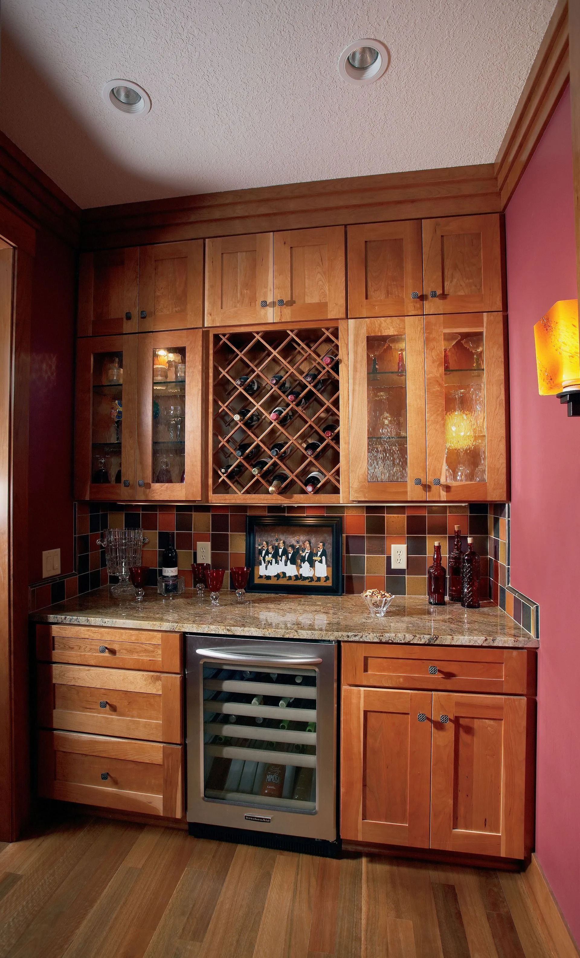 Wooden home bar with wine fridge, glass cabinets, wine rack, and granite countertop.