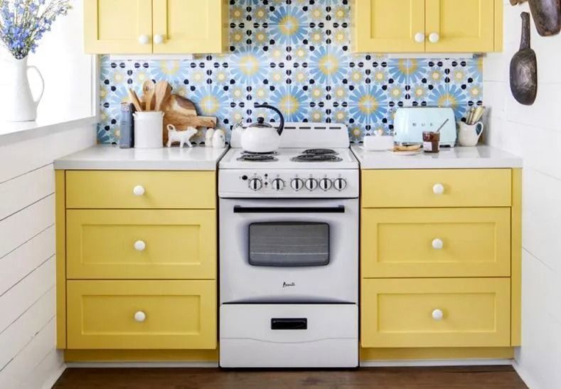 Yellow kitchen cabinets surround a white stove and countertop. Blue and yellow tile backsplash.