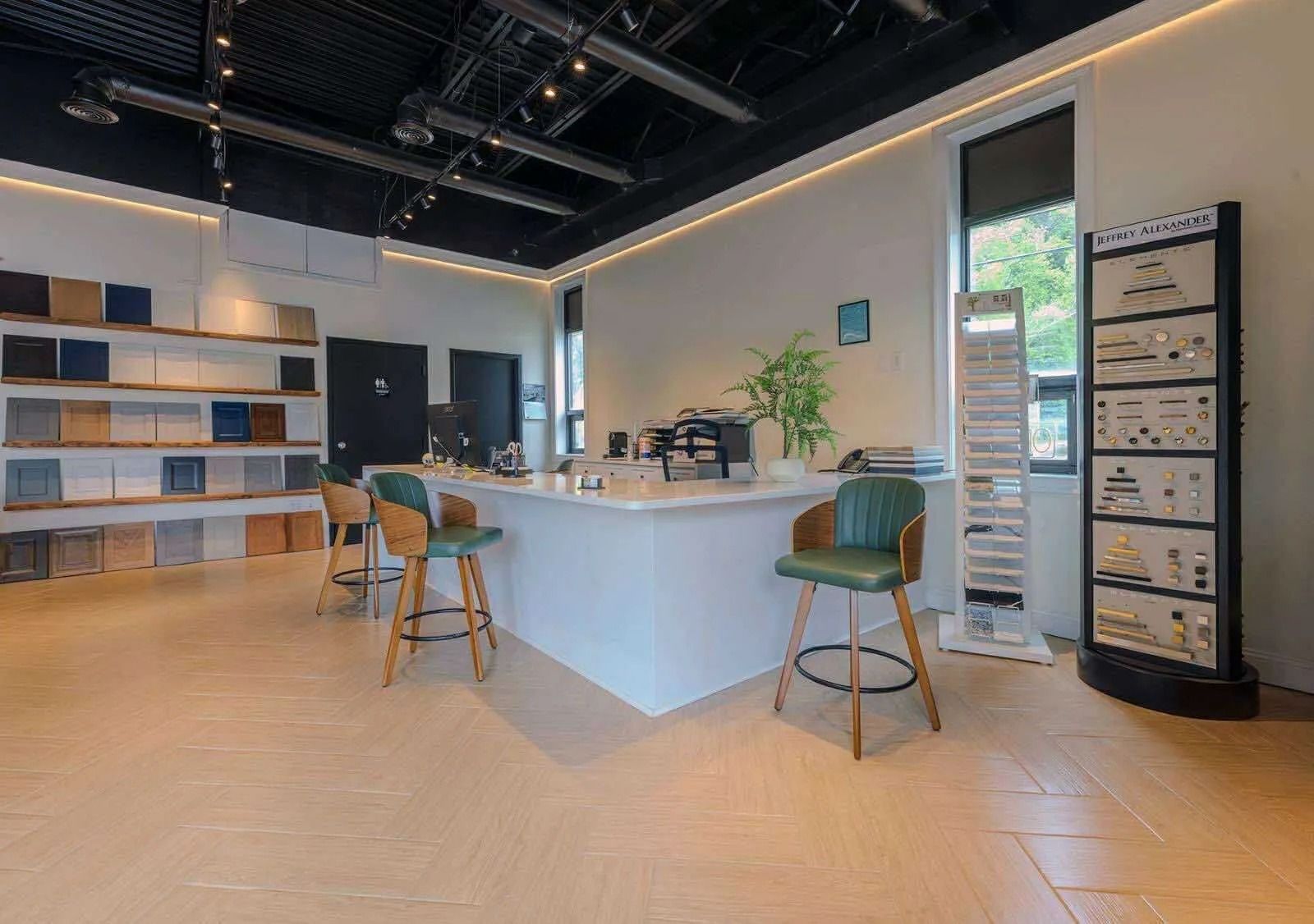 Interior of a showroom with a white counter and green bar stools. Product displays and samples are visible.