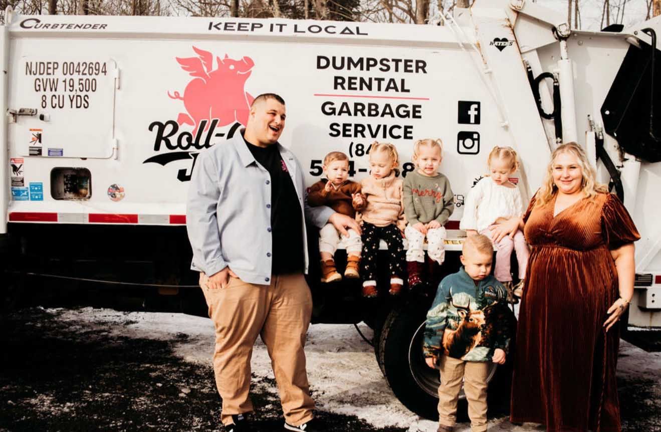 Family posing in front of a garbage truck that says “Roll-Off Joe’s” with their rental and service information.