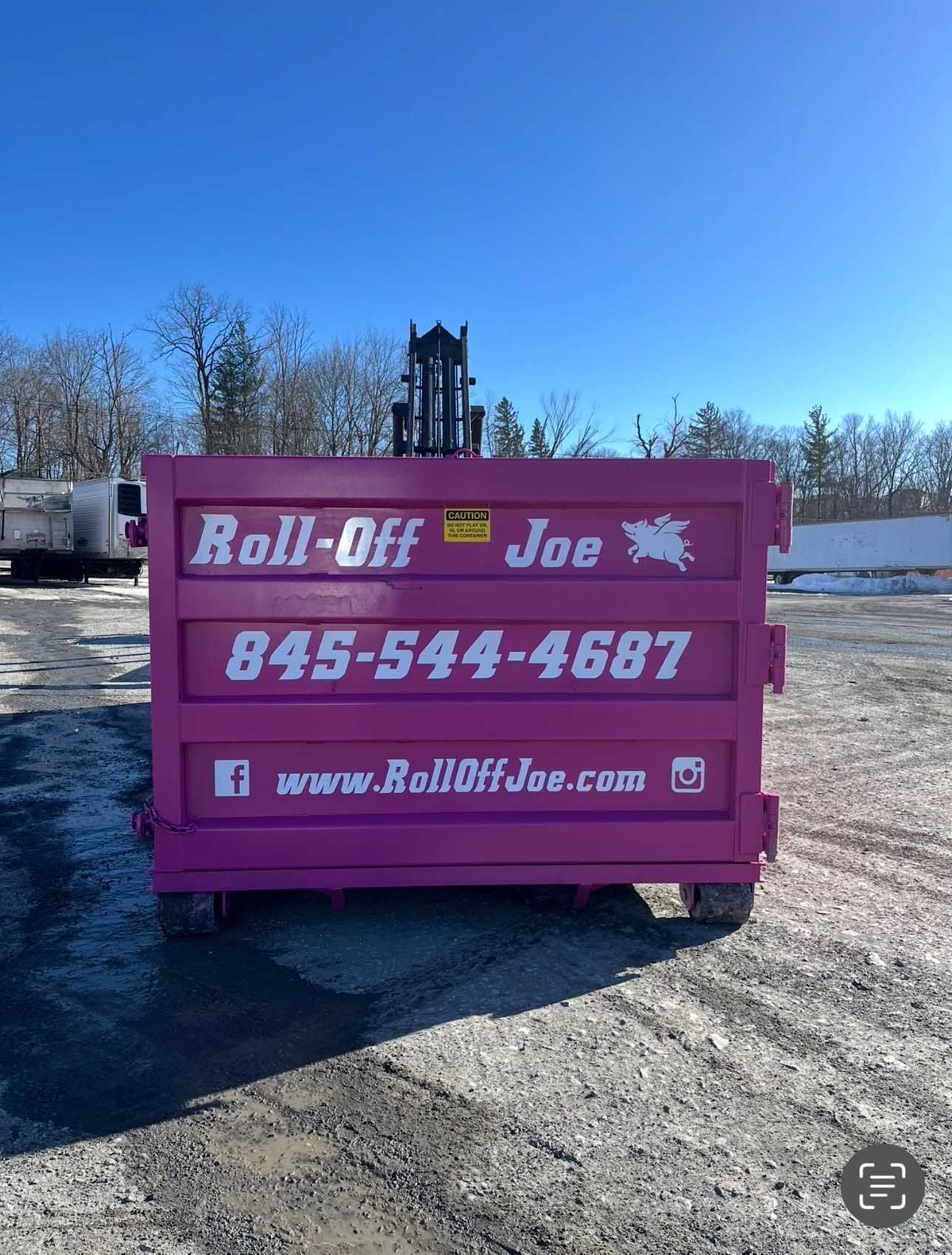 Pink Roll-Off Joe dumpster with phone number and website on a gravel lot under a blue sky.