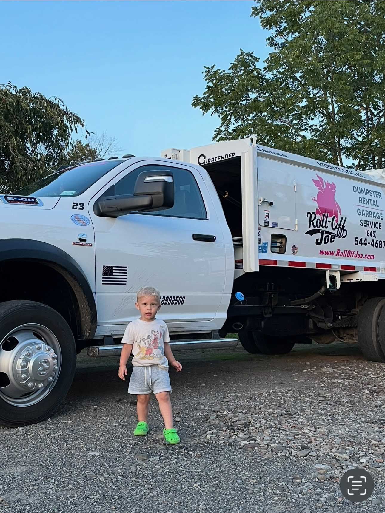 Child standing near a white dump truck, gravel lot.