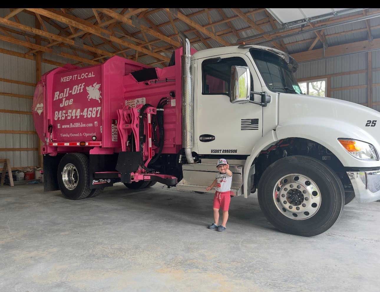 Pink and white garbage truck next to a young child in a garage.