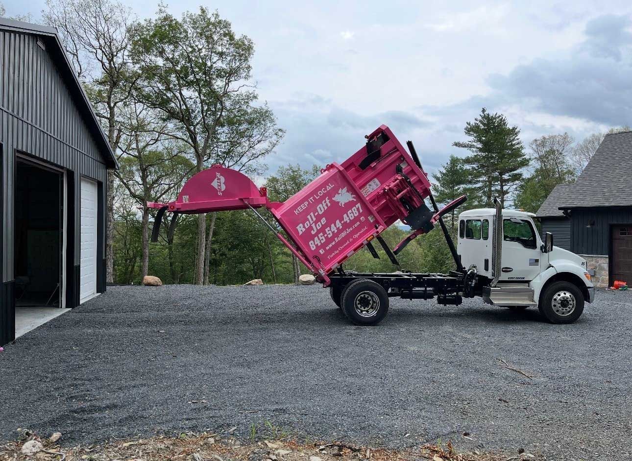 Pink dump truck unloading gravel in front of a building with garage doors.