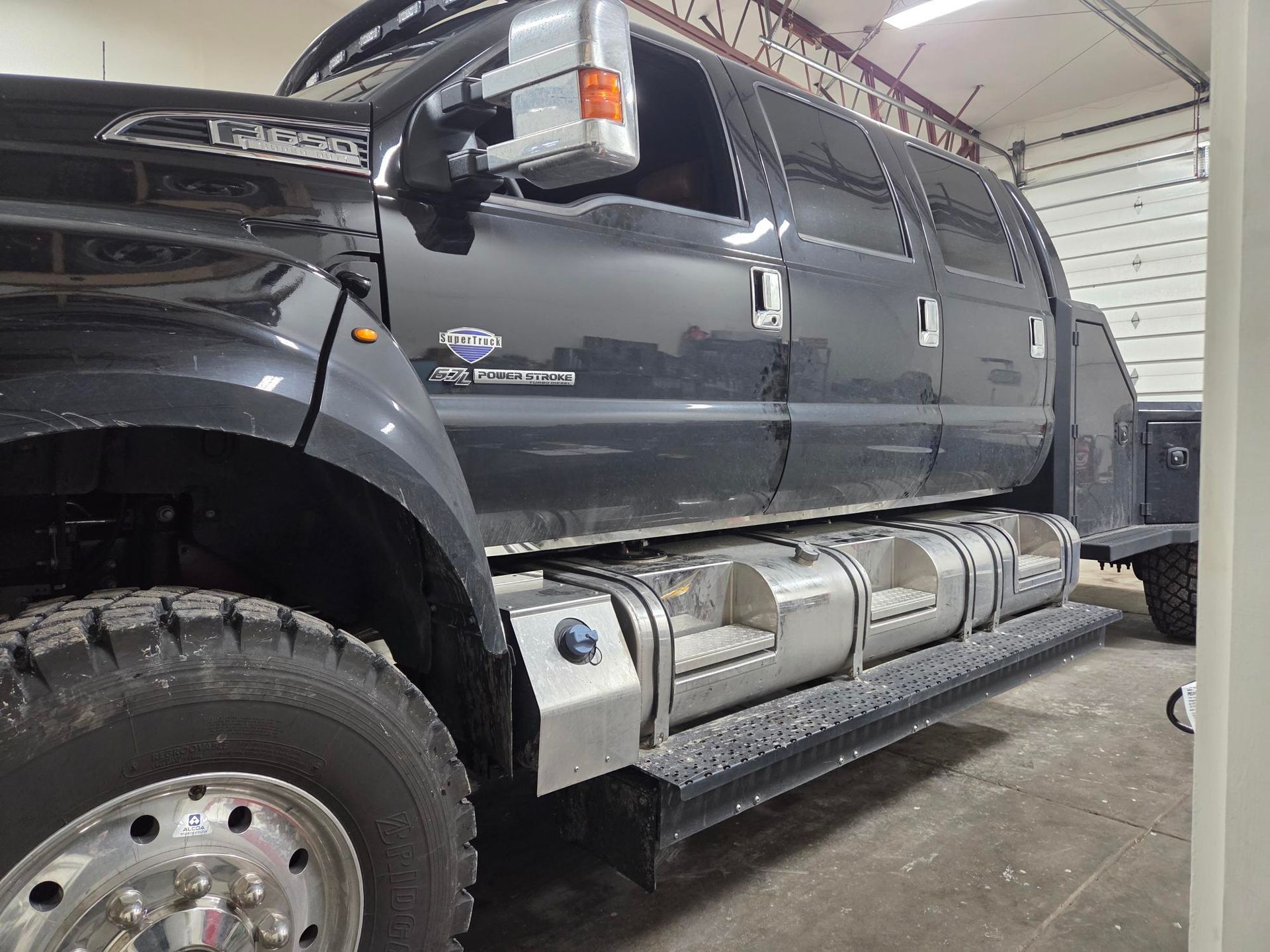 Black Ford F-650 Super Duty truck with extended cab and large tires, parked in a garage.