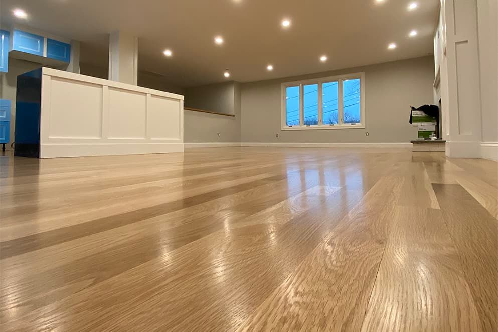 A large empty room with hardwood floors and a kitchen in the background.