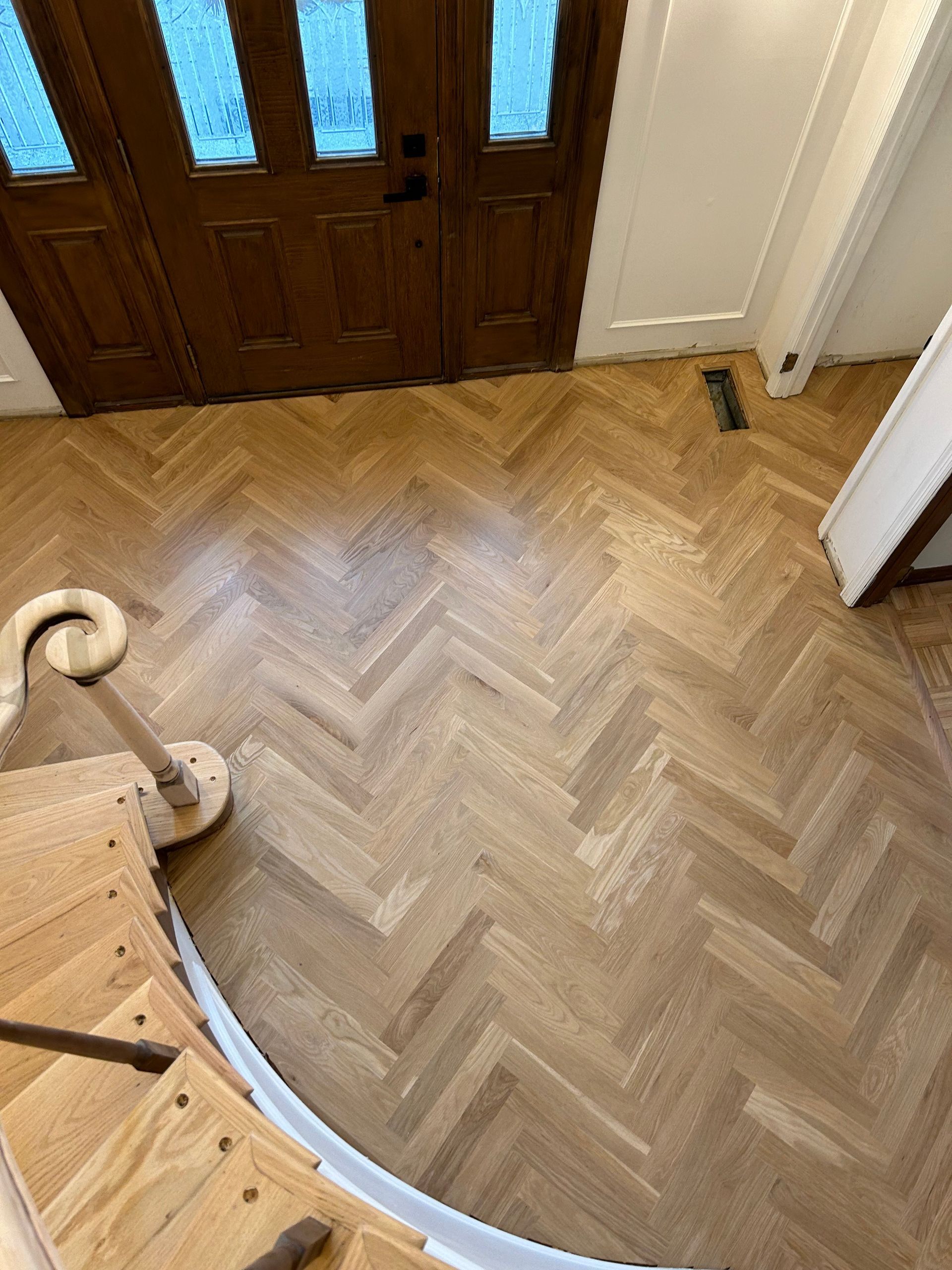 A wooden floor with a herringbone pattern and stairs in a hallway.