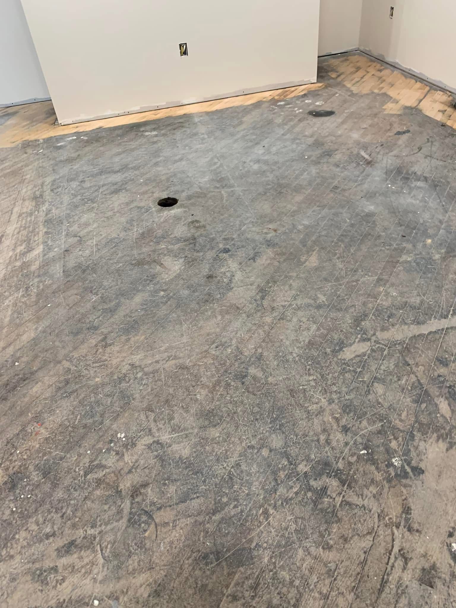 A dirty floor in a room with a hole in the middle of it.